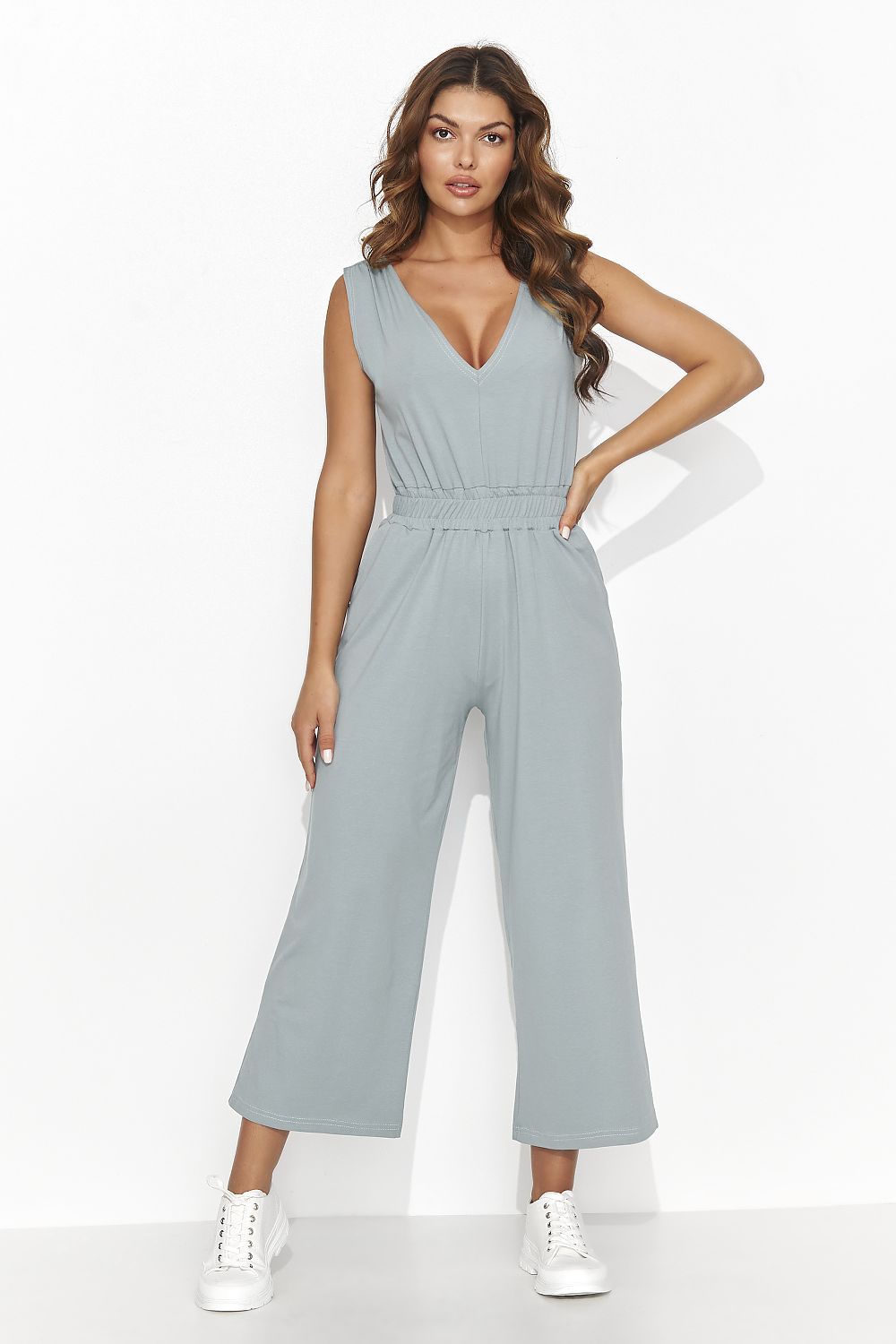 Vrouw draagt een gebreide Flare &amp; Flow Knit Dream jumpsuit in mintgroen, combineert met rieten tas en zonnehoed op het strand